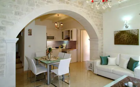 Un elegante soggiorno con un **arco in pietra moderno** che separa la zona pranzo dalla cucina. Divano bianco, quadri e lampadario di cristallo.