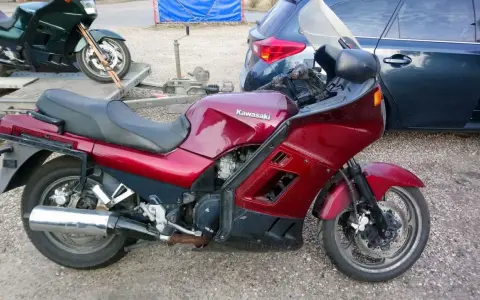 Czerwony motocykl Kawasaki GTR 1000 na przyczepce, obok ciemny samochód.