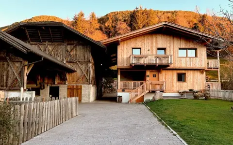 Maso Gallo Rosso: un'accogliente casa in legno e un fienile rustico immersi nel paesaggio alpino al tramonto.