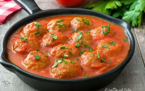 Polpette di lenticchie in salsa di pomodoro, guarnite con prezzemolo fresco, servite in una padella nera su un tavolo di legno.