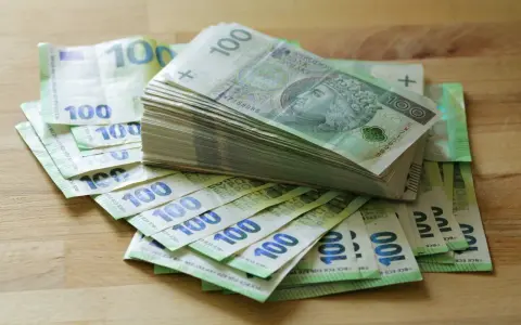 Stos banknotów 100 zł i 100 euro na drewnianym blacie. Może to być kwota na zasiłek stały.