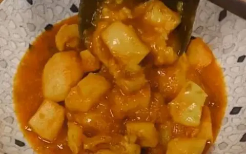 Un plato de papas con choco en una salsa naranja, servido en un cuenco con un patrón de puntos.