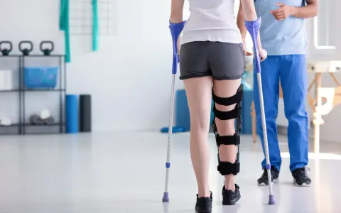 Fizjoterapeuta pomaga pacjentce z ortezą na nodze, ucząc ją, jak dopasować kule do wzrostu.