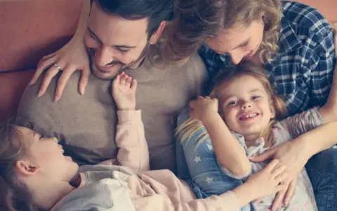 Glückliche Familie kuschelt auf dem Sofa. Zwei Elternteile umarmen ihre zwei Kinder, die sich an sie schmiegen.
