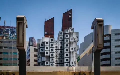 Iconica Nakagin Capsule Tower, un capolavoro di architettura modulare con capsule cubiche impilate, si staglia contro il cielo azzurro.