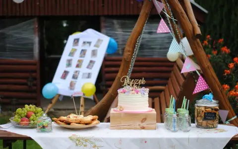 Na stole na roczek kładzie się tort, owoce, ciasteczka i słodkości. Dekoracje tworzą girlandy i zdjęcia.