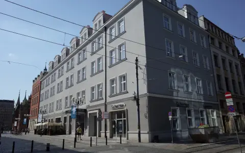 Elegancki hotel Korona Wrocław z szarym frontem i białymi oknami, na tle błękitnego nieba.