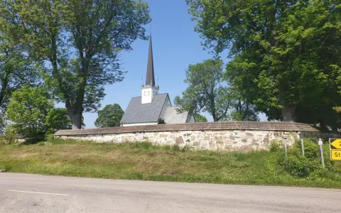 Kyrka med spira bakom stenmur och träd. En skylt visar "2 St". Kanske en vy från Hamar, Norge.