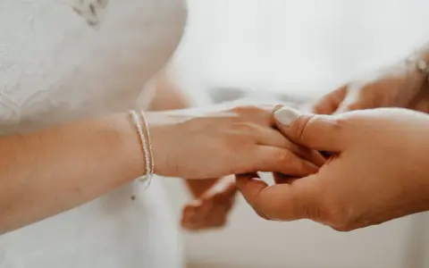 Delikatna bransoletka ślubna zdobi dłoń panny młodej, podczas gdy druga osoba delikatnie ją poprawia.