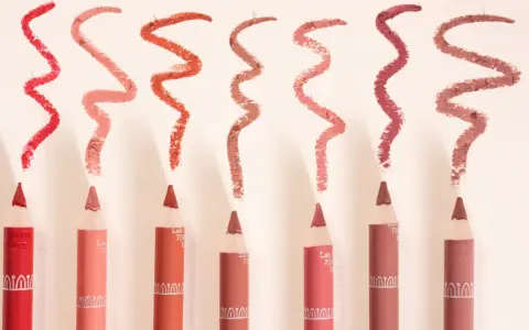 Plusieurs crayons à lèvres de différentes teintes, avec des échantillons de leur utilisation en traits ondulés.