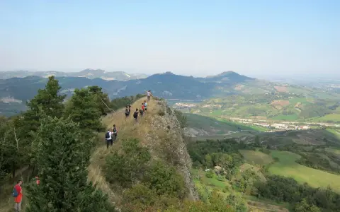 Un gruppo di escursionisti fa trekking su un crinale roccioso con vista panoramica sulle colline verdi, un'avventura indimenticabile vicino a Rimini.