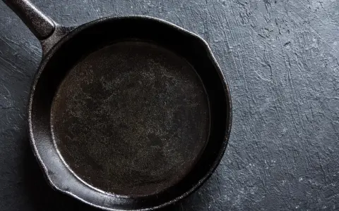 Eine schwarze Stahlpfanne, bereit für das Einbrennen, liegt auf einer dunklen, texturierten Oberfläche.