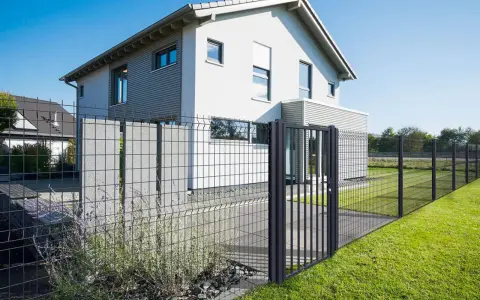 Maison moderne avec portail et pose grillage rigide, délimitant un jardin verdoyant.