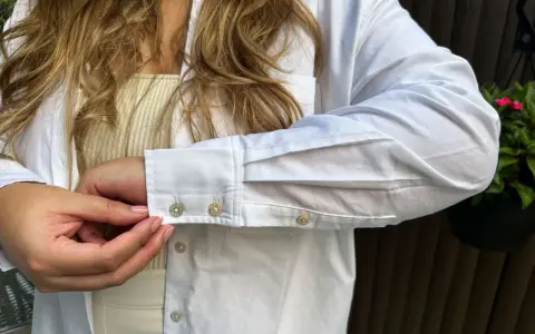 Sotto una camicia bianca, un top a coste color crema. Dettagli sui polsini con gemelli.