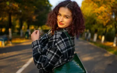 Dziewczyna w kratę, co to za styl? Ciepła flanela i zielona torebka na tle jesiennego parku.