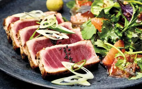 Tataki de atún perfectamente sellado, servido con una ensalada fresca de cítricos y hojas verdes.