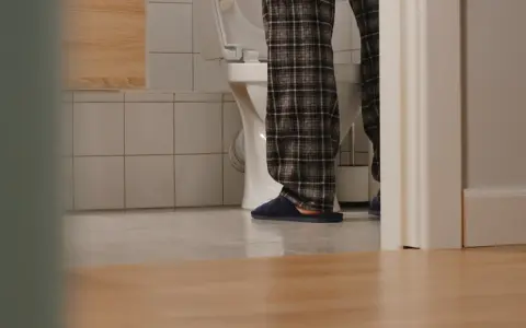 Osoba w piżamie stoi przy toalecie, doświadczając problemu z oddawaniem moczu.