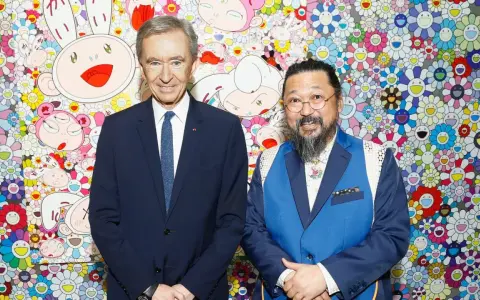 Two billionaire art collectors, Bernard Arnault and Takashi Murakami, pose in front of Murakami's signature smiling flower art.