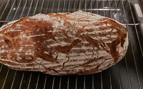 Frisch gebackenes Sauerteigbrot mit knuspriger Kruste auf einem Rost. Perfekt, um Hefe durch Sauerteig zu ersetzen!