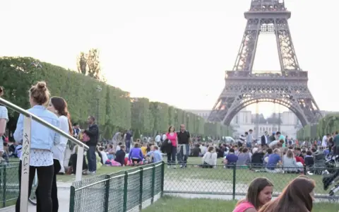 Gente disfrutando de un día soleado en París, con la Torre Eiffel de fondo. Un momento perfecto para la bise en France.
