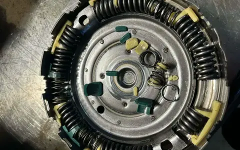 Zużyte elementy sprzęgła powershift: połamane zielone wkładki i sprężyny, objawy zużycia widoczne na metalowych częściach.
