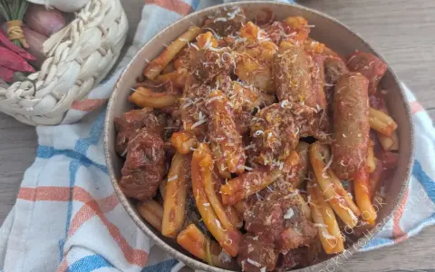 Herzhaftes Pasta Ragu mit Fleischstücken und geriebenem Käse, serviert in einer Schüssel auf einem karierten Tuch. Daneben ein Korb mit Knoblauch, Schalotten und Chilis.