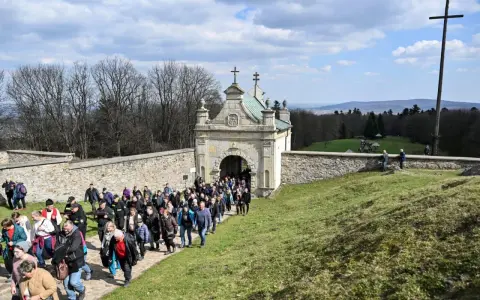 Pielgrzymka wchodzi przez zabytkową bramę. W oddali widać krzyż i piękne krajobrazy, które są nowa słupia atrakcje.