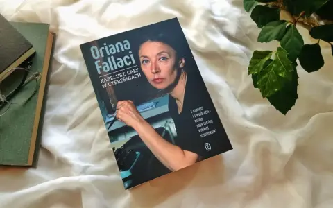 Książka "Kapelusz cały w czereśniach" Oriany Fallaci leży obok okularów i innych książek.