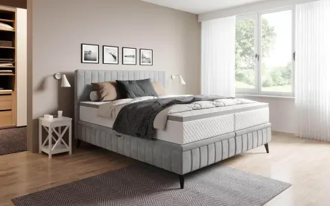 Sovrum med en stor säng i grått tyg. En fin balans att blanda beige och grått inredning med detaljer i trä och svarta tavlor på väggen.