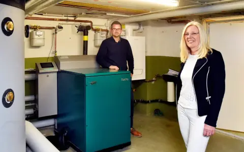Mann und Frau stehen neben einem grünen Nano BHKW-Gerät in einem Heizungsraum.