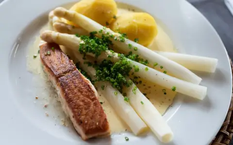 Ein Stück Lachs mit Spargel, Kartoffeln und Sauce Hollandaise. Der Spargel ist mit Schnittlauch bestreut.