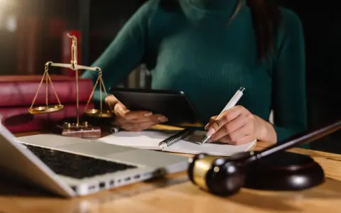Prawniczka analizuje dokumenty, pilnując, by nie przegapić ostatniego przedawnienia długu. Na biurku waga sprawiedliwości, laptop i młotek sędziowski.