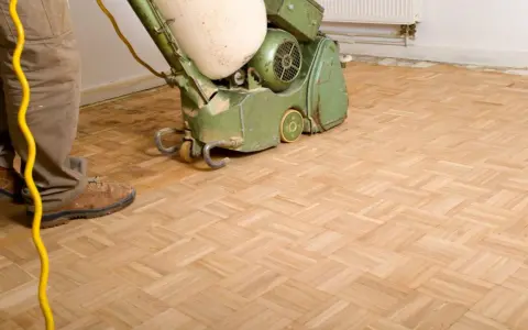 Mann bearbeitet einen Parkettboden mit einer Schleifmaschine. Der Boden schleifen ist ein wichtiger Schritt zur Erneuerung.