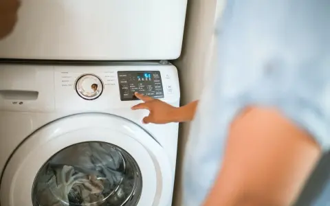 Dłoń naciska przycisk na panelu sterowania pralki, wybierając opcję "Eco Warm". Czy pralka sama podgrzewa wodę? Tak, ta opcja to umożliwia.