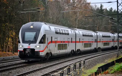 Ein moderner Doppelstockzug der Deutschen Bahn fährt durch eine herbstliche Landschaft. Die roten Streifen am Zug heben sich vom silbernen Lack ab.