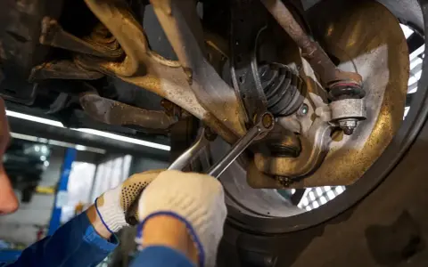 Mechanik dokręca śrubę w zawieszeniu samochodu. Widać elementy układu kierowniczego i amortyzator.