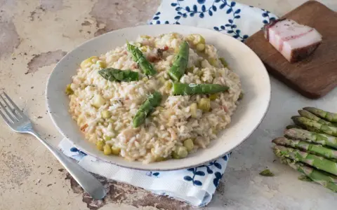Un cremoso risotto con asparagi e pancetta, guarnito con punte di asparagi freschi e una spolverata di parmigiano.