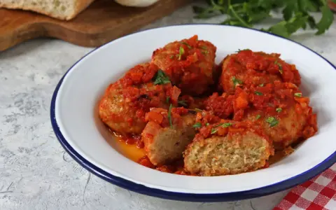 Polpette di pane succulente in salsa di pomodoro, guarnite con prezzemolo fresco. Un piatto casalingo che profuma di tradizione.