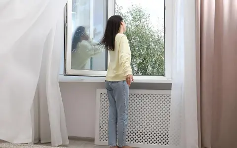 Mujer abre ventana para ventilar la casa en invierno. Reflejo en el cristal muestra a otra persona.