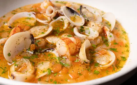 Sopa de mariscos con gambas, calamares y almejas en un caldo dorado con perejil.