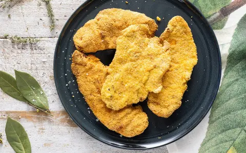 Cotolette dorate e croccanti, perfette cotolette in friggitrice ad aria, servite su un piatto scuro con erbe aromatiche e foglie di alloro.
