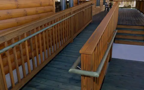 A wooden wheelchair ramp with railings curves around a log cabin. This shows how to build a wheelchair ramp for accessibility.