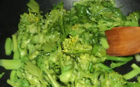 Cime di rapa salteados en sartén con una cuchara de madera. Verduras verdes vibrantes y frescas, listas para ser disfrutadas.