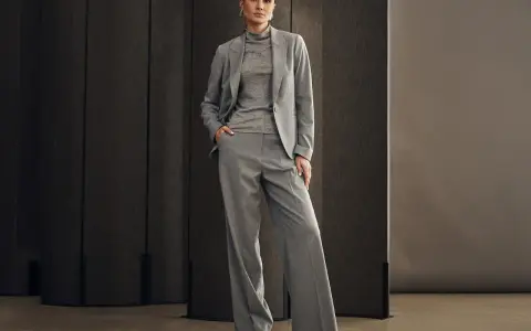 Elegancka kobieta w szarym garniturze, idealnym na wesele. Spodnie z szerokimi nogawkami i marynarka tworzą stylowy zestaw.