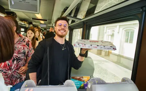 Uśmiechnięty mężczyzna z pizzą w ręku w pociągu relacji Kraków-Praga.