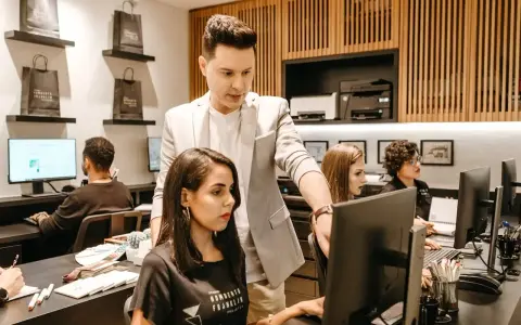 Koordynator w jasnej marynarce wskazuje coś na monitorze pracownicy.