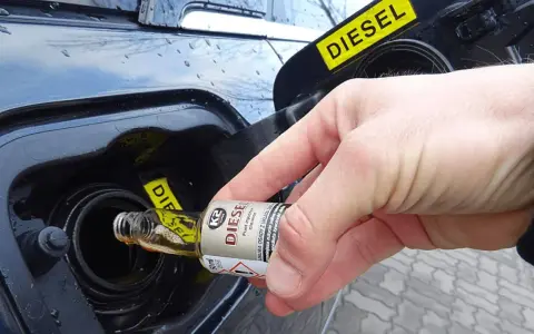 Dłoń wlewa dodatek do benzyny do baku samochodu z napisem DIESEL.