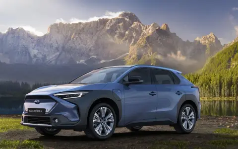 Niebieski Subaru Solterra stoi nad jeziorem z górami w tle.