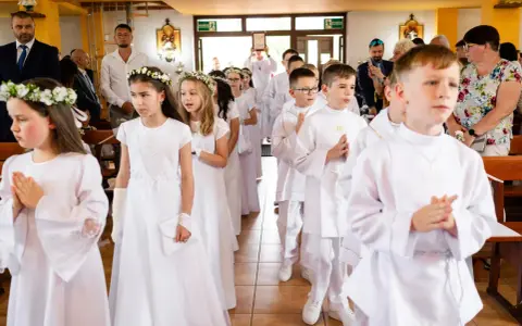 Dzieci w białych strojach, dziewczynki z wiankami, chłopcy z medalikami, przygotowują się do przyjęcia sakramentu, co to jest komunia święta.