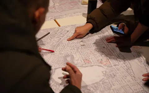 Menschen diskutieren auf einer Karte, die Details der Stadt zeigt. Sie planen die monitoring soziale stadtentwicklung, markieren Bereiche und nutzen ein Smartphone.